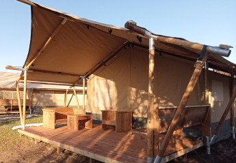 Tenda safari con veranda in legno e area salotto esterna, ideale per un'esperienza di campeggio.