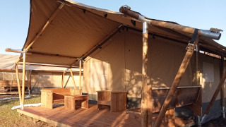 Tenda safari con veranda in legno e area salotto esterna, ideale per un'esperienza di campeggio.