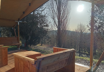 Udsigt fra Safari-telt ved Camping La Perle i Frankrig med træmøbler og sollys over træerne.