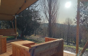 View from Safari tent at Camping La Perle in France with wooden furniture and sunlight over trees.
