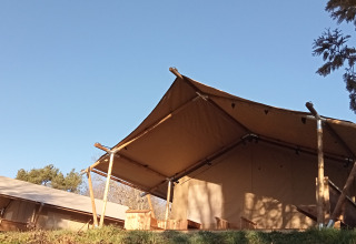 Safari-Zelt auf dem Campingplatz La Perle in Frankreich mit Holzkonstruktion unter blauem Himmel.