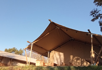 Tienda safari en Camping La Perle en Francia, con estructura de madera y toldo bajo un cielo despejado.