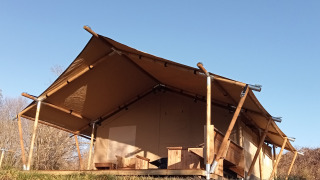 Safari tent with wooden frame and canvas roof set in nature underneath a clear blue sky during daytime.