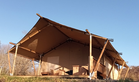 Tenda safari con struttura in legno e tetto in tela immersa nella natura sotto un cielo azzurro limpido.