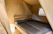 Interieur van een safaritent op Camping La Perle in Frankrijk met tweepersoonsbed en nachtkastje.