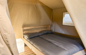 Indvendig udsigt af en safari telt på Camping La Perle i Frankrig med en dobbeltseng og et natbord.
