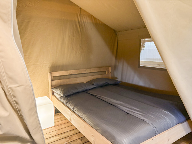 Binnenzicht van een safaritent op Camping La Perle in Frankrijk met dubbel bed en nachtkastje.
