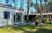 Forest Lodge De Mooie Plek op Bospark Markelo in Nederland, moderne lodge met terras tussen hoge bomen.