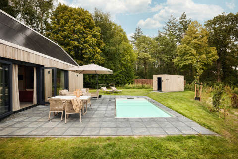 Außenansicht der Unbrick One Lodge mit Sauna, Pool, Terrasse, Gartenmöbeln und grüner Umgebung.