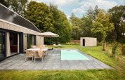 Udendørs udsigt over Unbrick One-lodgen med sauna, pool, terrasse, havemøbler og grønne omgivelser.