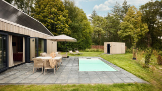Außenansicht der Unbrick One Lodge mit Sauna, Pool, Terrasse, Gartenmöbeln und grüner Umgebung.