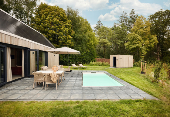 Buitenaanzicht van Unbrick One lodge met sauna, zwembad, terras, tuinmeubels en groene omgeving.