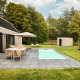 Außenansicht der Unbrick One Lodge mit Sauna, Pool, Terrasse, Gartenmöbeln und grüner Umgebung.