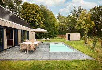 Vue extérieure du lodge Unbrick One avec sauna, piscine, terrasse, mobilier de jardin et cadre verdoyant.