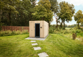 Un lodge moderno in legno con porta nera, posizionato su un prato verde e circondato da alberi e natura.