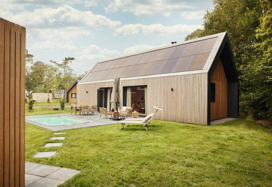 Foto einer modernen Lodge mit großen Solarpanelen auf dem Dach, Pool und Terrasse im grünen Garten.