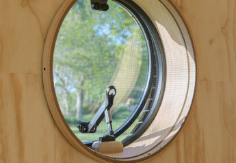 Finestra circolare con vista sugli alberi dall'interno della Wrap house al Resort de Parel nei Paesi Bassi.