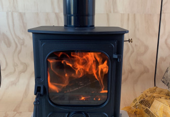 Schwarzer Holzofen mit sichtbarem Feuer auf Fliesen, Innenraum im Wrap house, Resort de Parel, Niederlande.