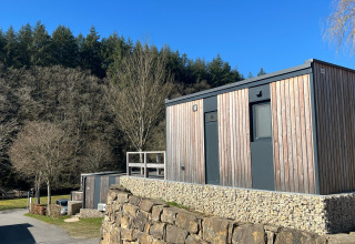 Kleine houten tiny house op een stenen fundering met bos op de achtergrond in Kohnenhof, Luxemburg.