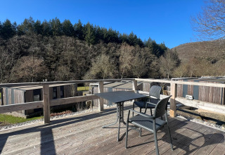 Vista da una terrazza in legno con tavolo e due sedie al Tiny House di Kohnenhof in Lussemburgo, circondato dalla foresta.