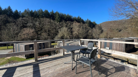 Udsigt fra træterrasse med bord og to stole ved Tiny House på Kohnenhof i Luxembourg, omgivet af skov.