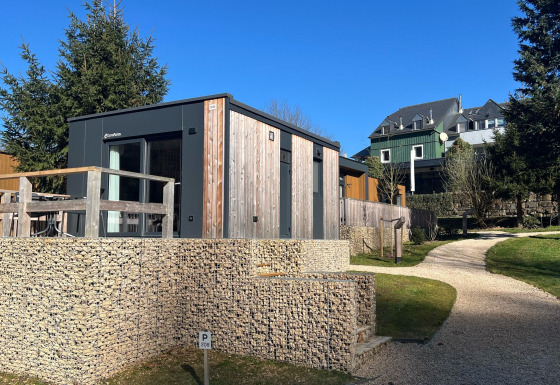 Modernes Tiny House in Kohnenhof, Luxemburg, mit Holz Fassade, Gartenweg und grünem Gelände bei Sonne.