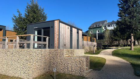 Tiny house moderna a Kohnenhof, in Lussemburgo, con terrazza in legno, sentiero e alberi intorno sotto il sole.