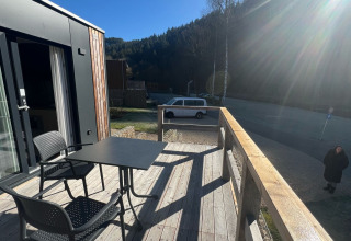 Terrazza in legno del Tiny House a Kohnenhof, Lussemburgo, con tavolo, sedie, auto e sole splendente.