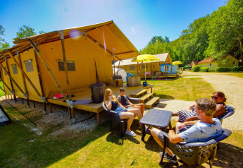 Family relaxing outside a Lodgetent Bordeaux safari tent on a sunny campsite with green surroundings.