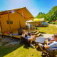 Familie nyder solskin foran en Lodgetent Bordeaux safaritelt på en campingplads omgivet af natur.