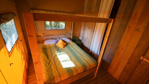 Schlafzimmer im Lodgetent Bordeaux auf La Draille in Frankreich mit Holzwänden und Doppelbett.