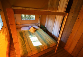 Dormitorio en la tienda Lodgetent Bordeaux de La Draille en Francia, con paredes de madera y cama acogedora.