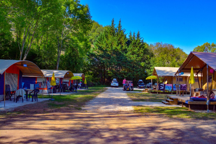 Safari tents at Lodgetent Bordeaux, La Draille, France, with green trees and a bright blue sky.