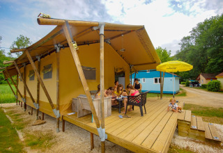 Familie isst gemeinsam draußen vor einem Safarizelt Lodgetent Bordeaux auf dem Campingplatz La Draille, Frankreich.