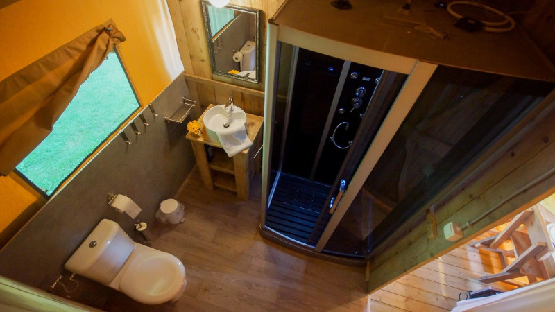 Bathroom inside safari tent Lodgetent Bordeaux at La Draille, France, featuring toilet, sink and shower.
