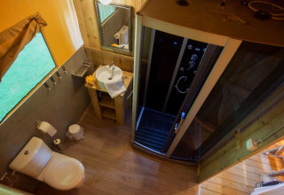 Baño dentro de la tienda safari Lodgetent Bordeaux en La Draille, Francia, con ducha, inodoro y lavabo.
