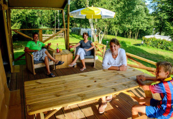 Family relaxing on the porch of a safari tent Lodgetent Bordeaux at La Draille campsite in France.
