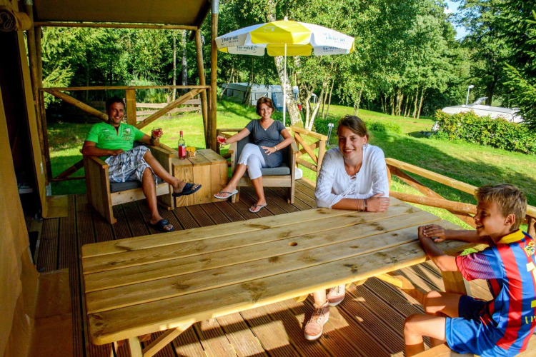 Family relaxing on the porch of a safari tent Lodgetent Bordeaux at La Draille campsite in France.