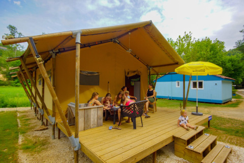 Familie entspannt auf der Terrasse eines Safarizelts Lodgetent Bordeaux auf dem Campingplatz La Draille in Frankreich.