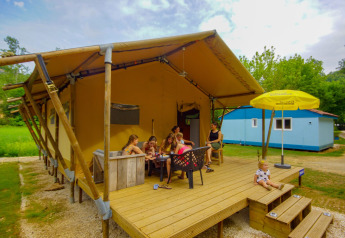 Familie hygger sig på terrassen foran en safaritelte Lodgetent Bordeaux på La Draille camping i Frankrig.
