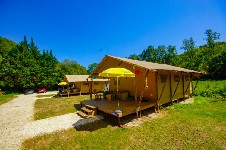 Safari tent Lodgetent Bordeaux at La Draille, France, with porch, yellow umbrella, and green natural setting.