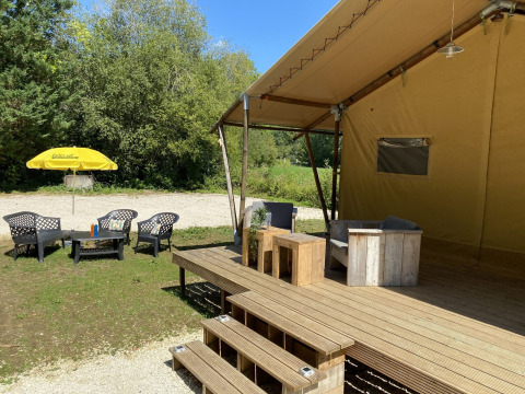 Zona de estar exterior en Lodgetent Bordeaux, La Draille, Francia, con terraza, sillas y sombrilla amarilla.