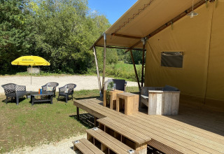 Zona de estar exterior en Lodgetent Bordeaux, La Draille, Francia, con terraza, sillas y sombrilla amarilla.