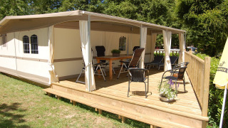 Tienda safari Glampingtent Cahors en La Draille, Francia, con terraza de madera cubierta, sillas y mesa al aire libre.