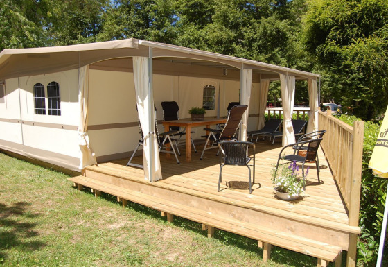 Tienda safari Glampingtent Cahors en La Draille, Francia, con terraza de madera cubierta, sillas y mesa al aire libre.