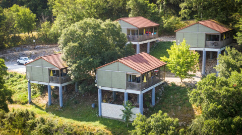 Cuatro cabañas elevadas con techos rojos y terrazas rodeadas de árboles en Chalet Belvedere, La Draille, Francia.