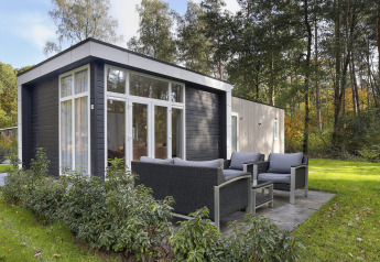 Moderne tiny house med terrasse og havemøbler i skovområde i Bospark Markelo, Holland, omgivet af natur.