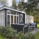 Moderne tiny house med terrasse og havemøbler i skovområde i Bospark Markelo, Holland, omgivet af natur.