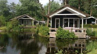 Dos pequeñas casas negras junto a un estanque en Lodge Meerkoet, Bospark Markelo, Países Bajos.