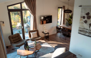 Bright, modern lodge interior with large windows, cozy chairs, wooden table, TV and inviting decor.